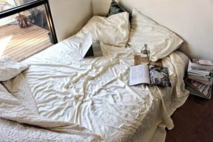 Bed with bamboo sheet and items like laptop, books, pillow lying on it