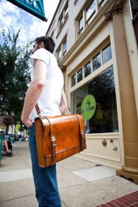 A man carrying leather messenger bag infront of a cafe