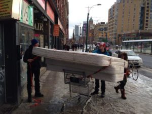 men trying to carry matress on shopping cart
